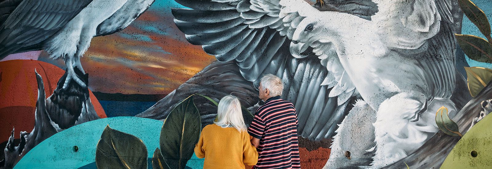 A man and a women looking at a painted mural banner image