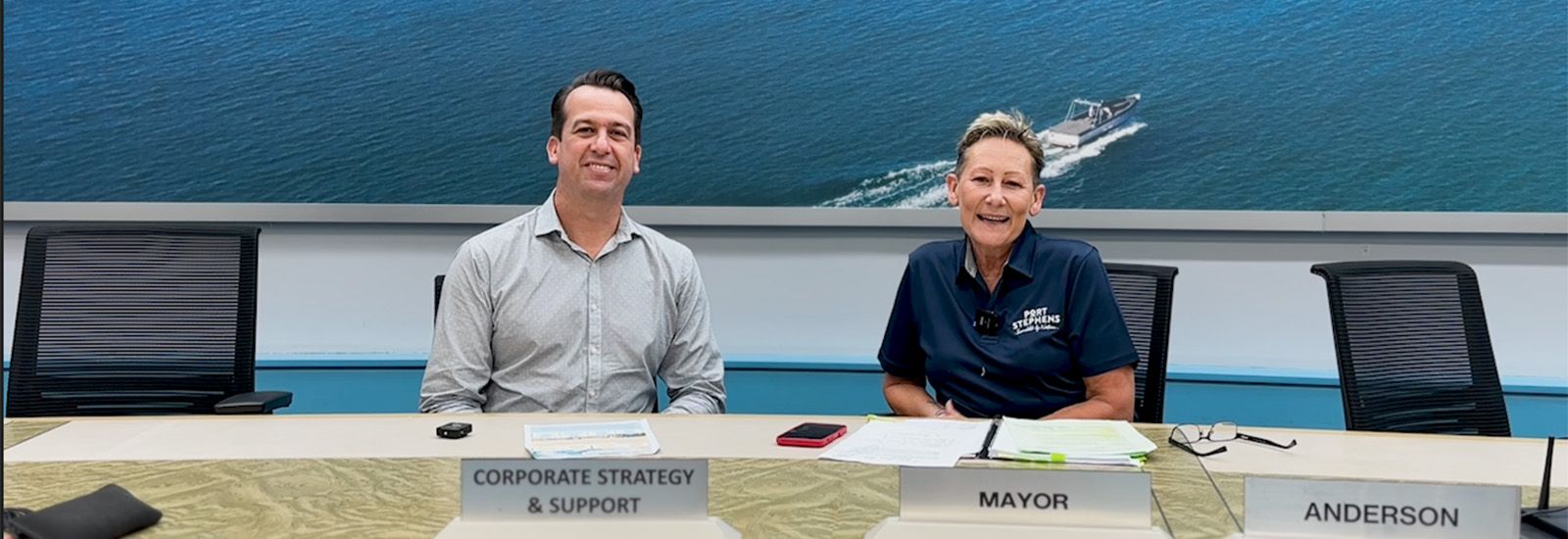 2 people smiling in front of a picture of water  banner image