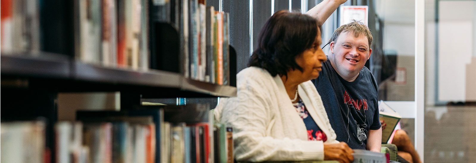 Young man waving sitting in a library banner image